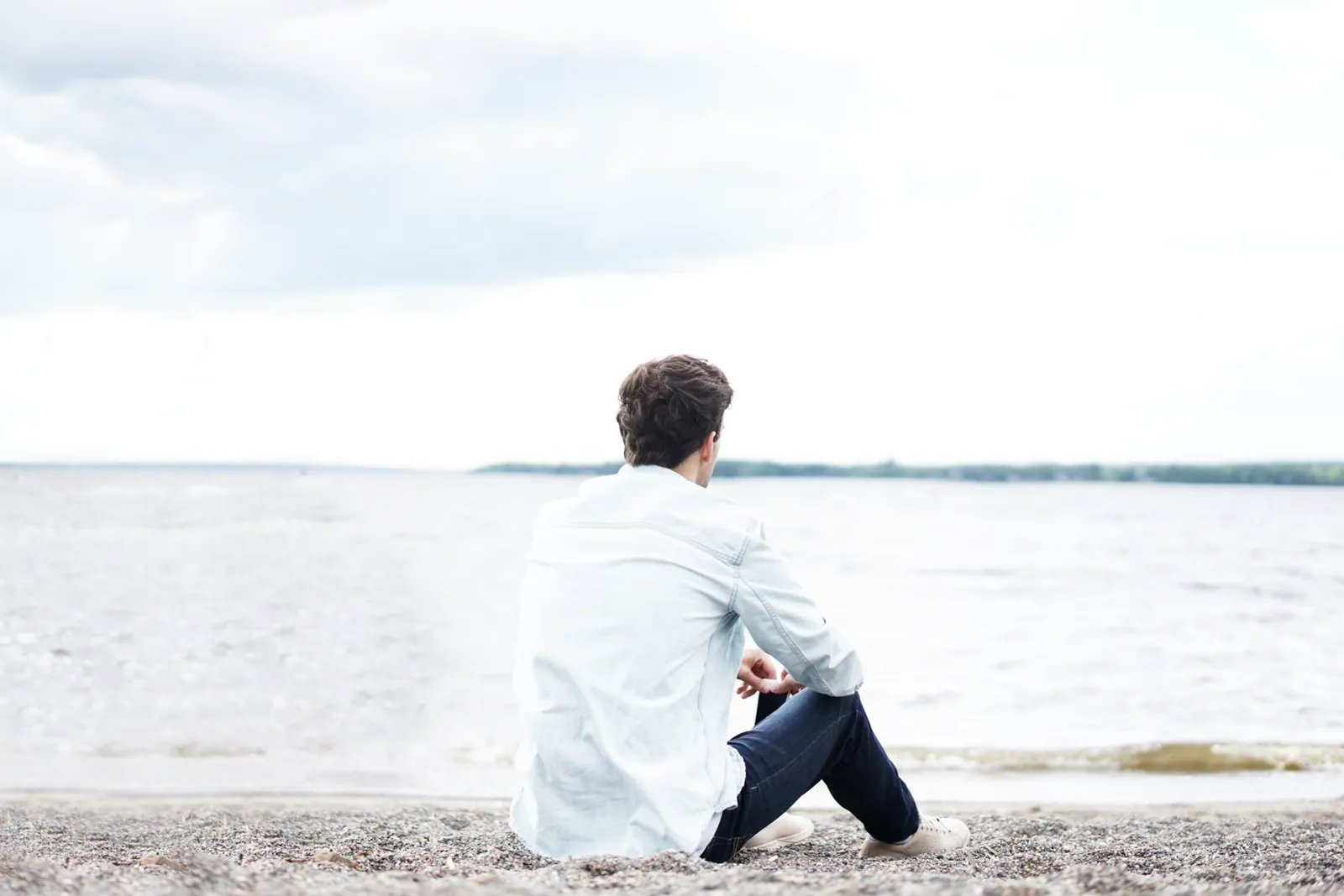 A person sits looking out at the sea from a beach.