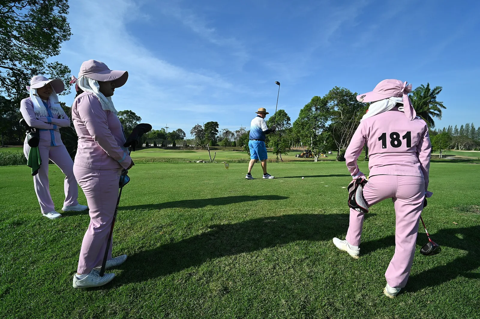A golfer tees off as others watch on a sunny course