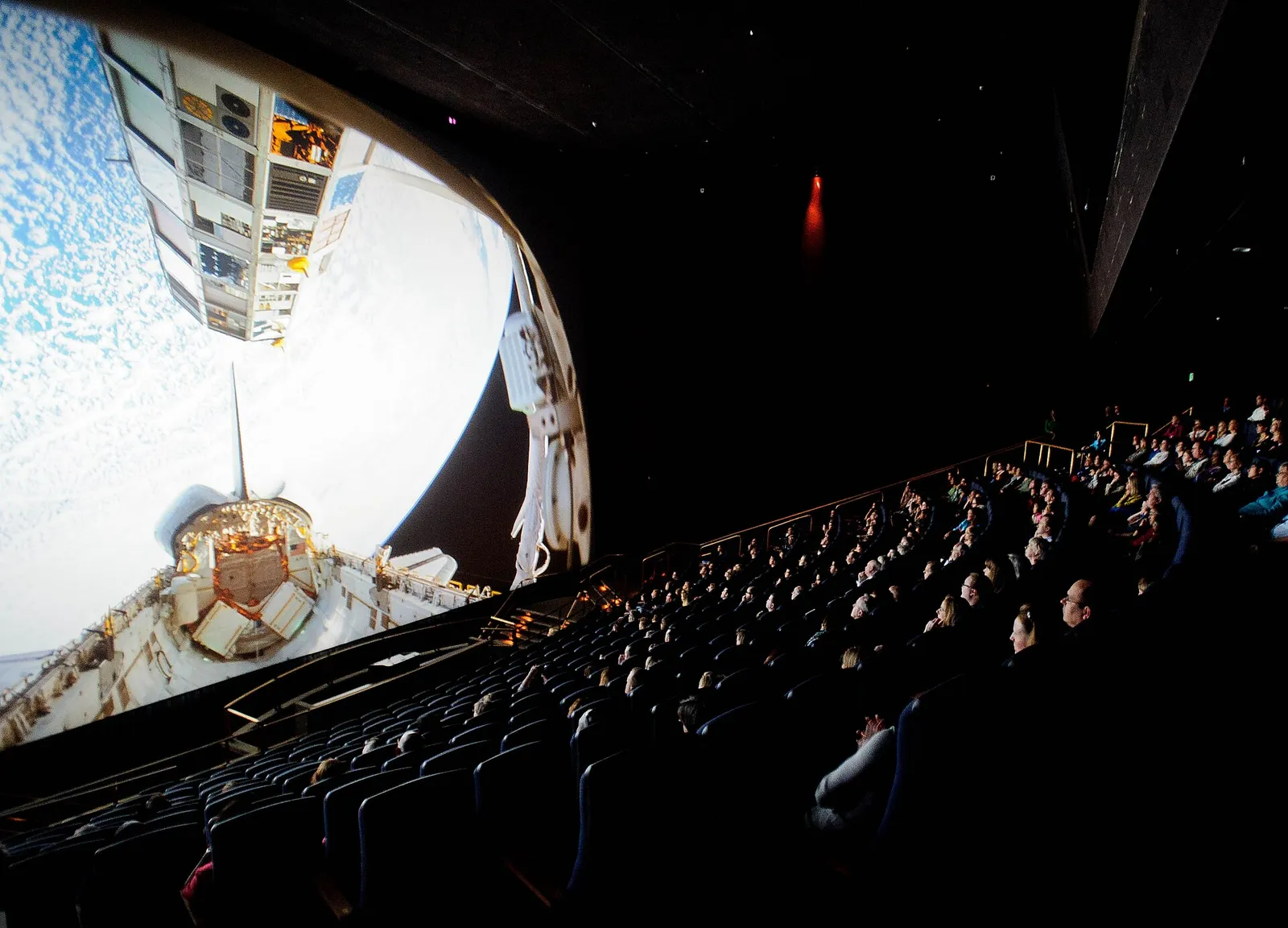 An audience watches a film on a large-format IMAX screen.