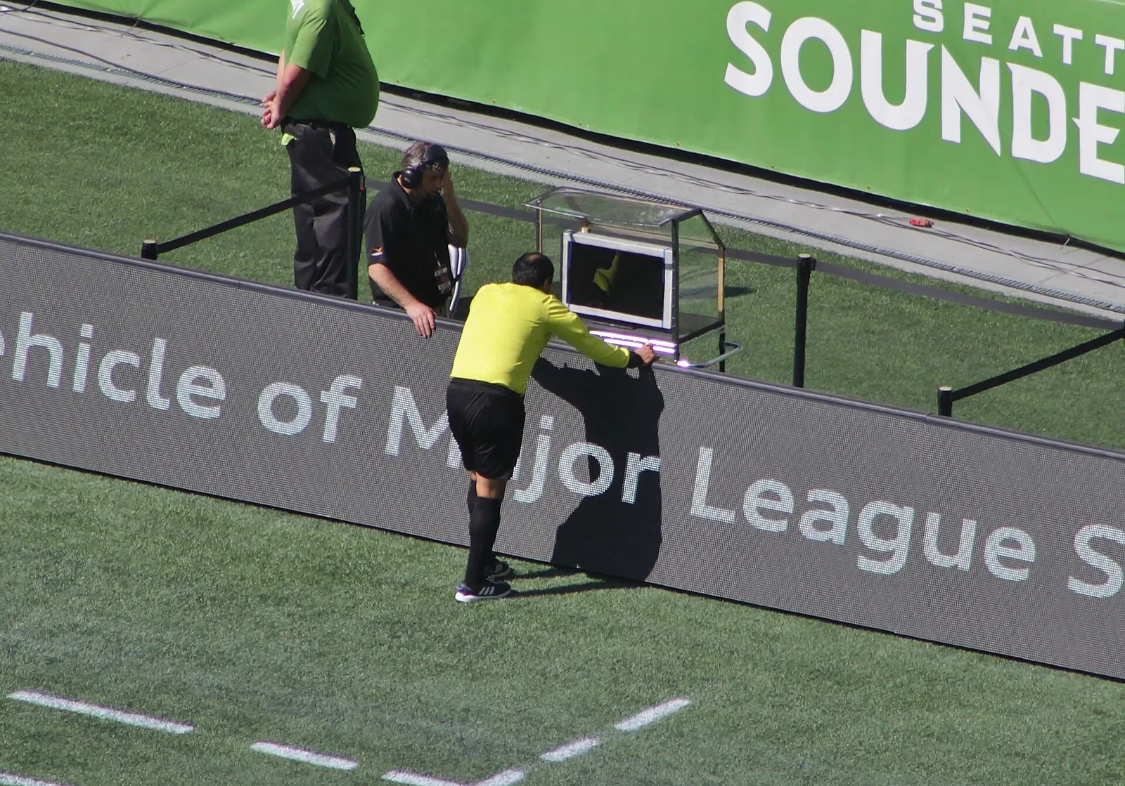 A referee reviews a play on a pitchside video (VAR) monitor.